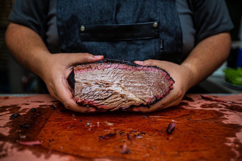 Close-up of hands holding a juicy smoked beef brisket on a wooden cutting board, showcasing rich texture.