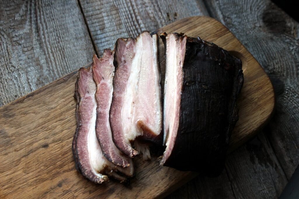 Close-up of smoked bacon slices on a rustic wooden board, showcasing delicious texture.