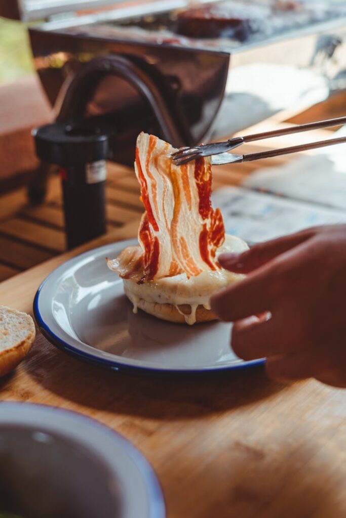 Crop anonymous person taking slice of delicious bacon from plate with yummy bread while having dinner